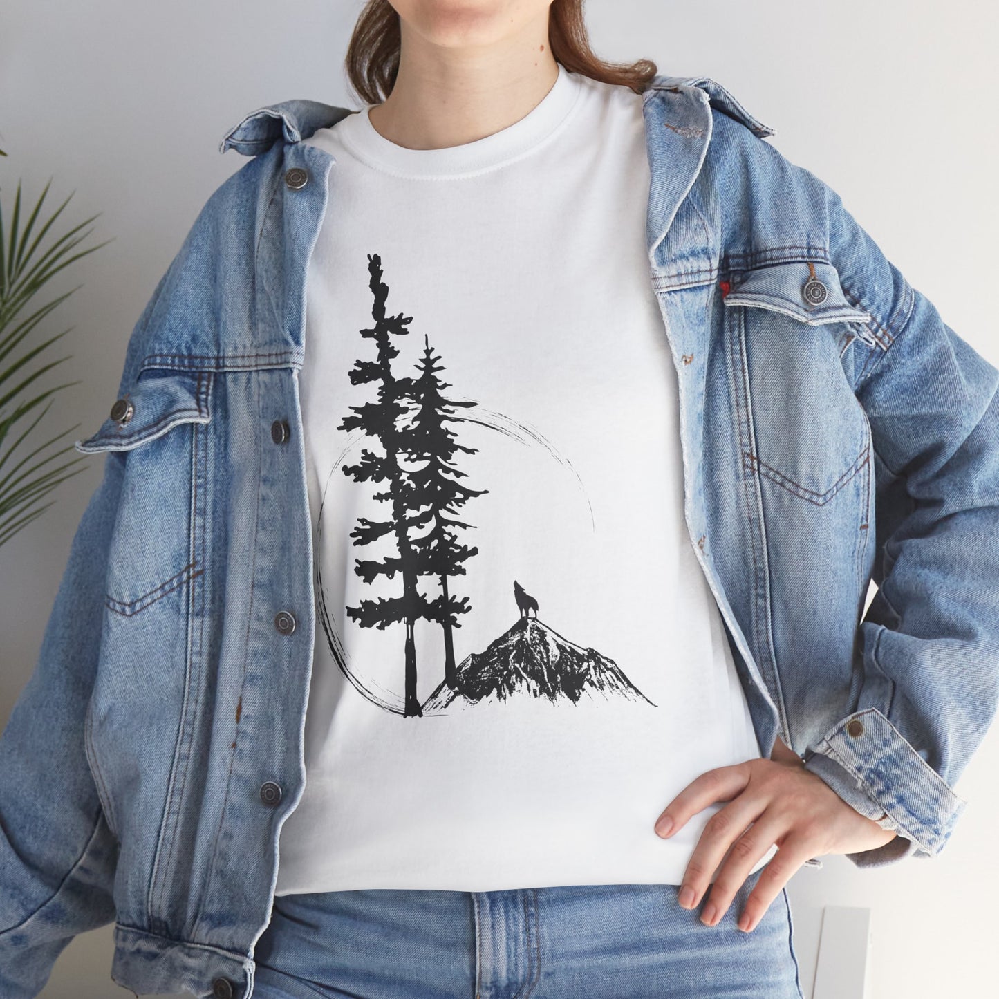 Person wearing a white t-shirt with a tree and mountain design, paired with a denim jacket.