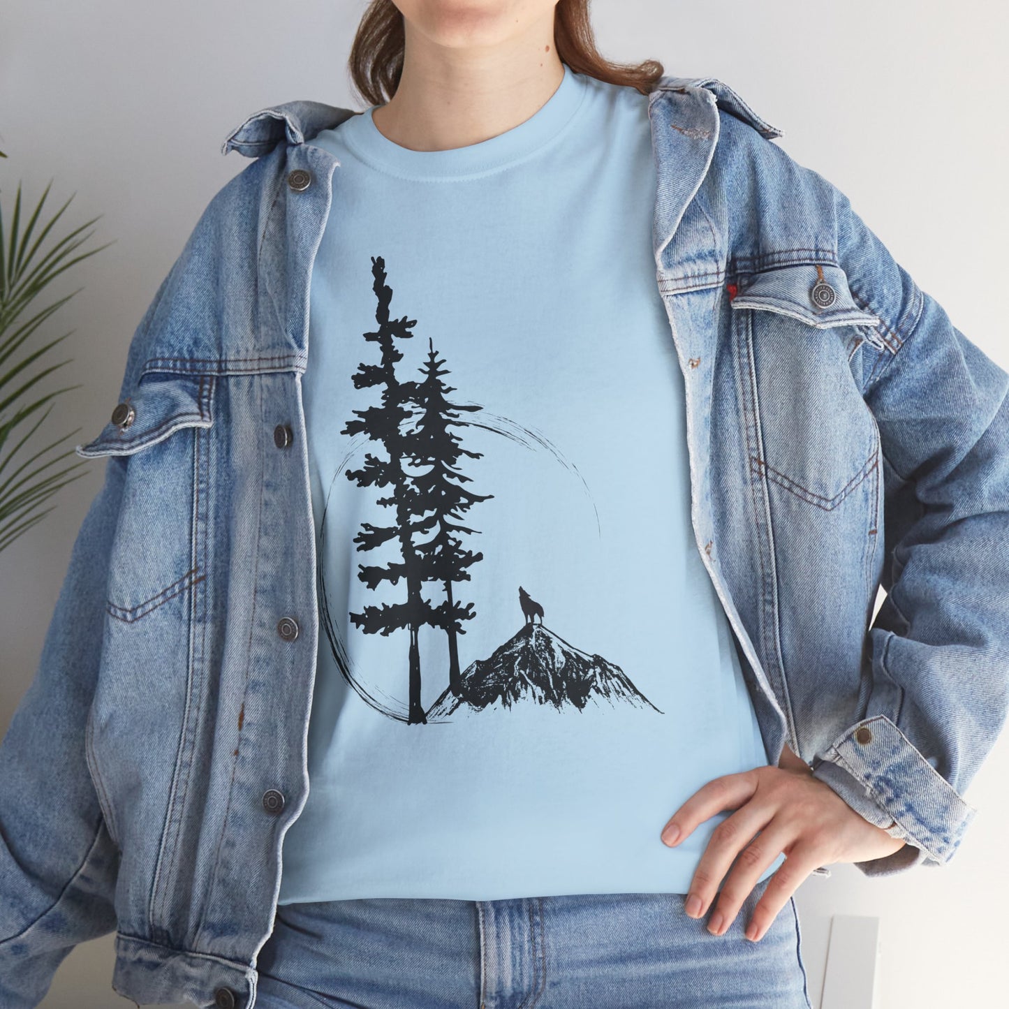 Person wearing a light blue t-shirt with a tree and mountain graphic, paired with a denim jacket.